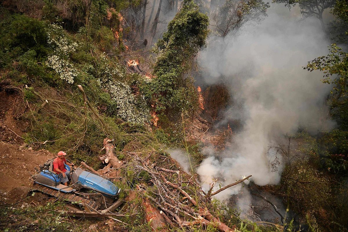 A man brings trees and branches together as fire crews attempt to build a controlled fire zone to prevent the blaze to reach the village of Kechries in North Evia, on August 5, 2021, near. - The blazes in Greece this week briefly cut off the main road leading to Athens and saw worrying fires break out in Olympia -- the birthplace of the Olympic Games that is usually crowded with tourists -- and on the island of Evia.