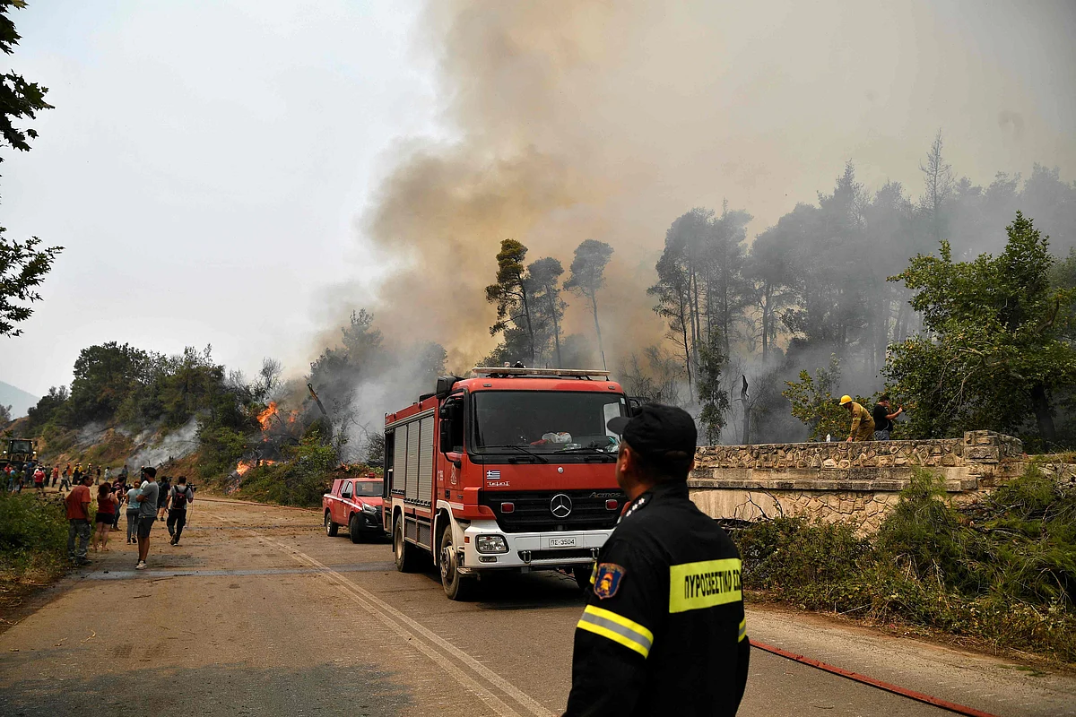 Fire crews and onlookers stand on a road during a wildfire on August 5, 2021, near the village of Kechries in North Evia. - The blazes in Greece this week briefly cut off the main road leading to Athens and saw worrying fires break out in Olympia -- the birthplace of the Olympic Games that is usually crowded with tourists -- and on the island of Evia.