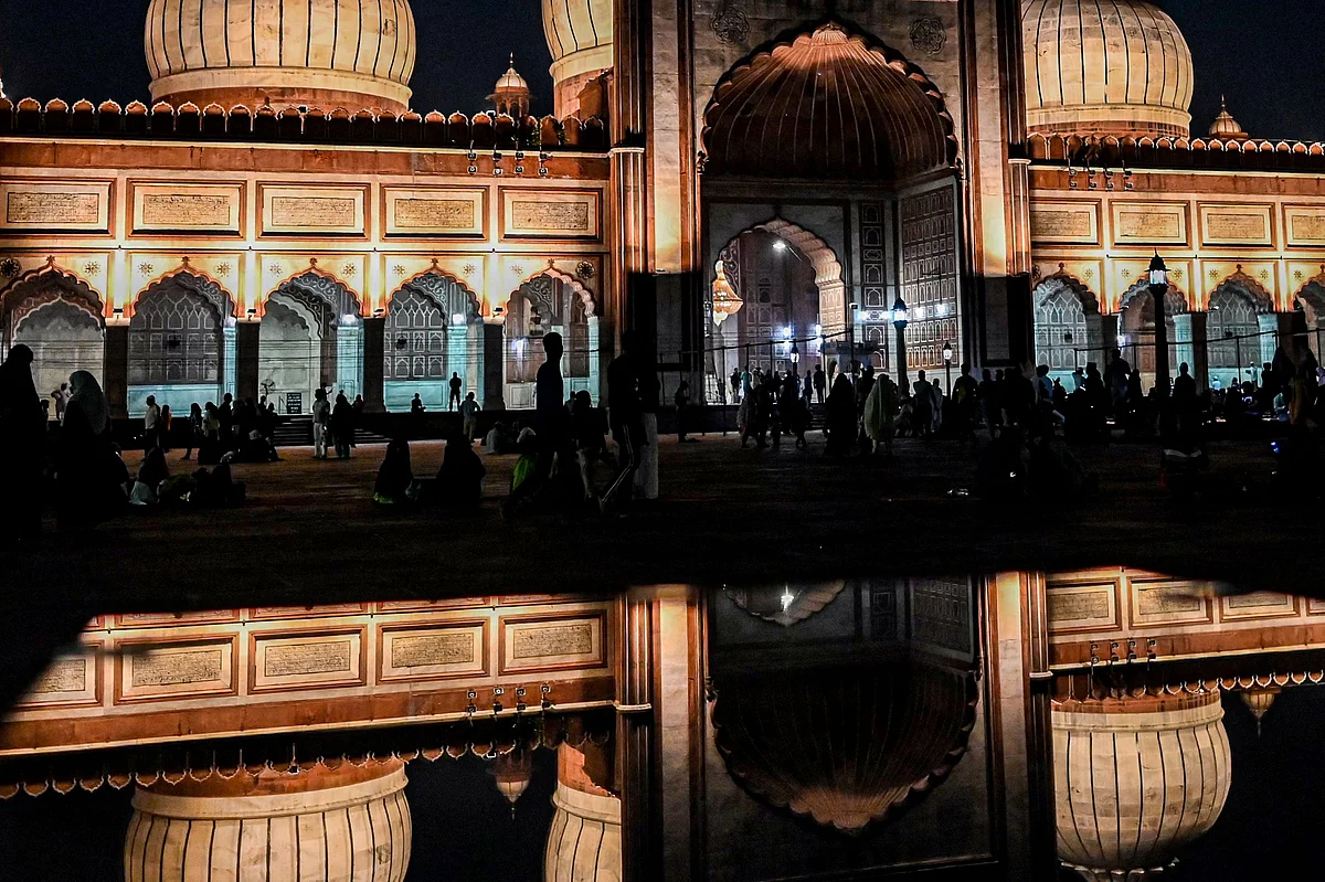 Muslim devotees and other visitors are silhouetted against the illuminated Jama Masjid Mosque on the eve of the start of holy fasting month of Ramadan in the old quarters of Delhi on April 2, 2022. (Photo by Sajjad HUSSAIN / AFP)