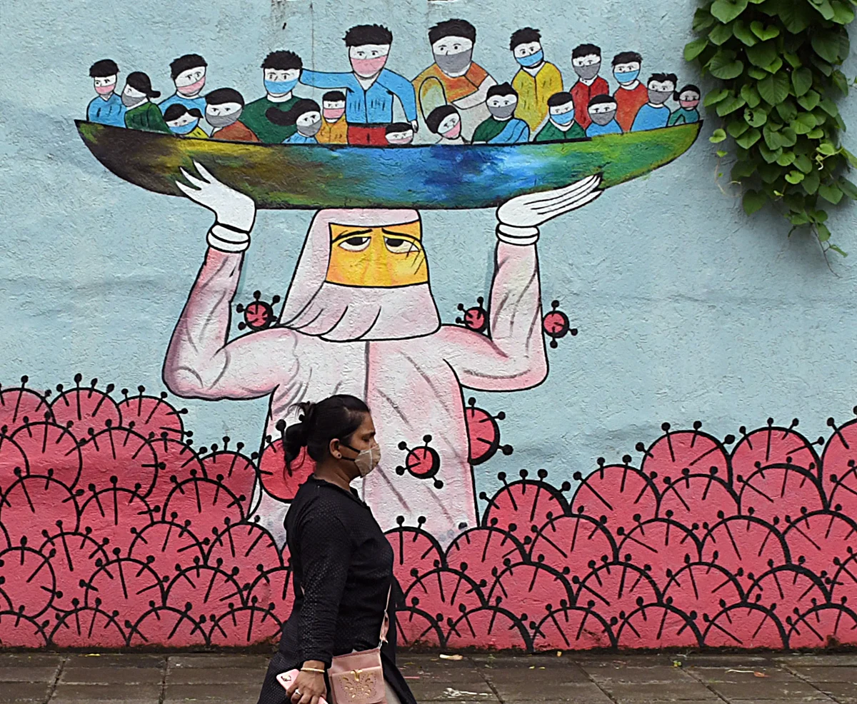 A woman wearing a protective mask walks past a wall graffiti creating awareness against COVID-19, at Navi Mumbai, in Thane.
