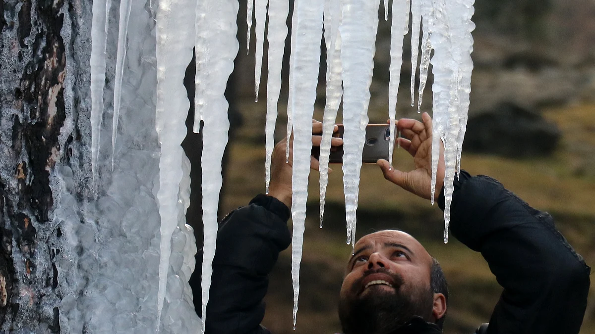 A man clicks icicles formed on a tree amid freezing cold weather conditions, in north Kashmir's Baramulla district on Saturday December 11, 2021.