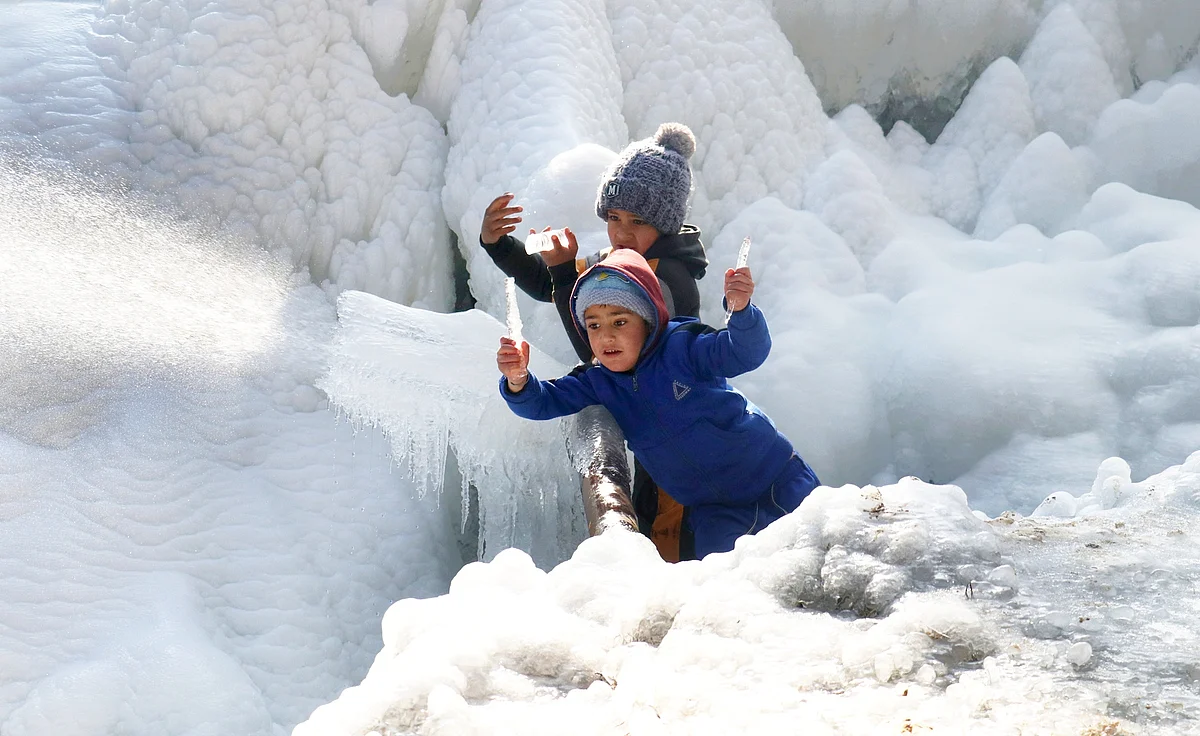 Children break icicles off a burst water pipe in north Kashmir's Baramulla on Tuesday December 20, 2021.