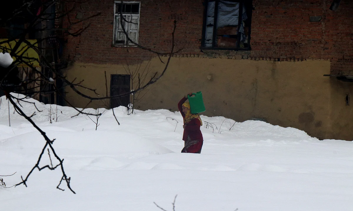 A woman braves chill and snowfall to collect water in north Kashmir's Drung area.