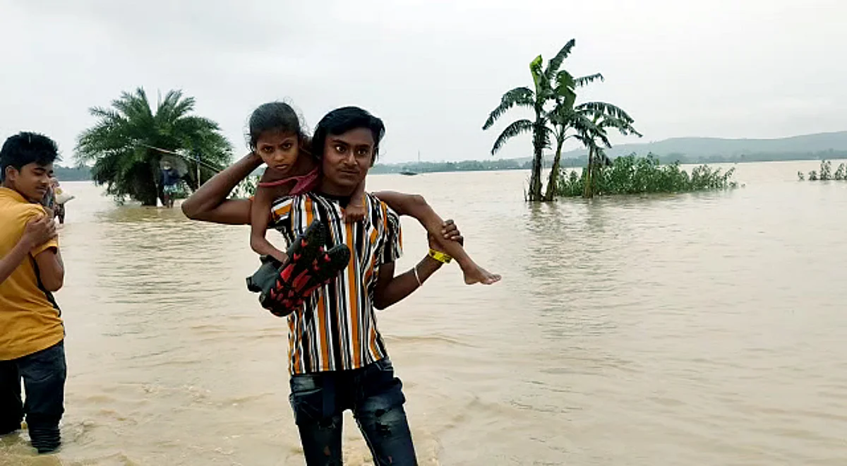 Nagaon, May 15: A man carries child on his shoulder wade through a waterlogged road to move to a safer place as Flood situation worsens in Assam triggered by incessant rainfall, in Nagaon on Tuesday.