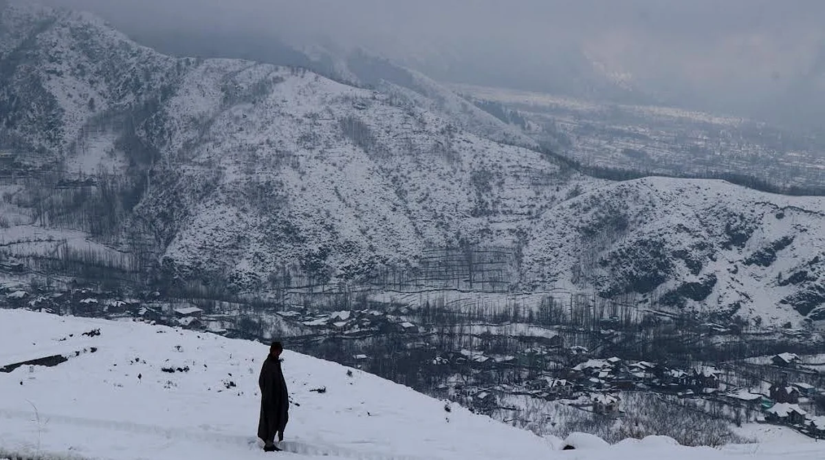 A boy stands on a hill on the outskirts of Srinagar overlooking the city with snow-covered Zabarwan hills in the backdrop, on Saturday 14 January 2023.