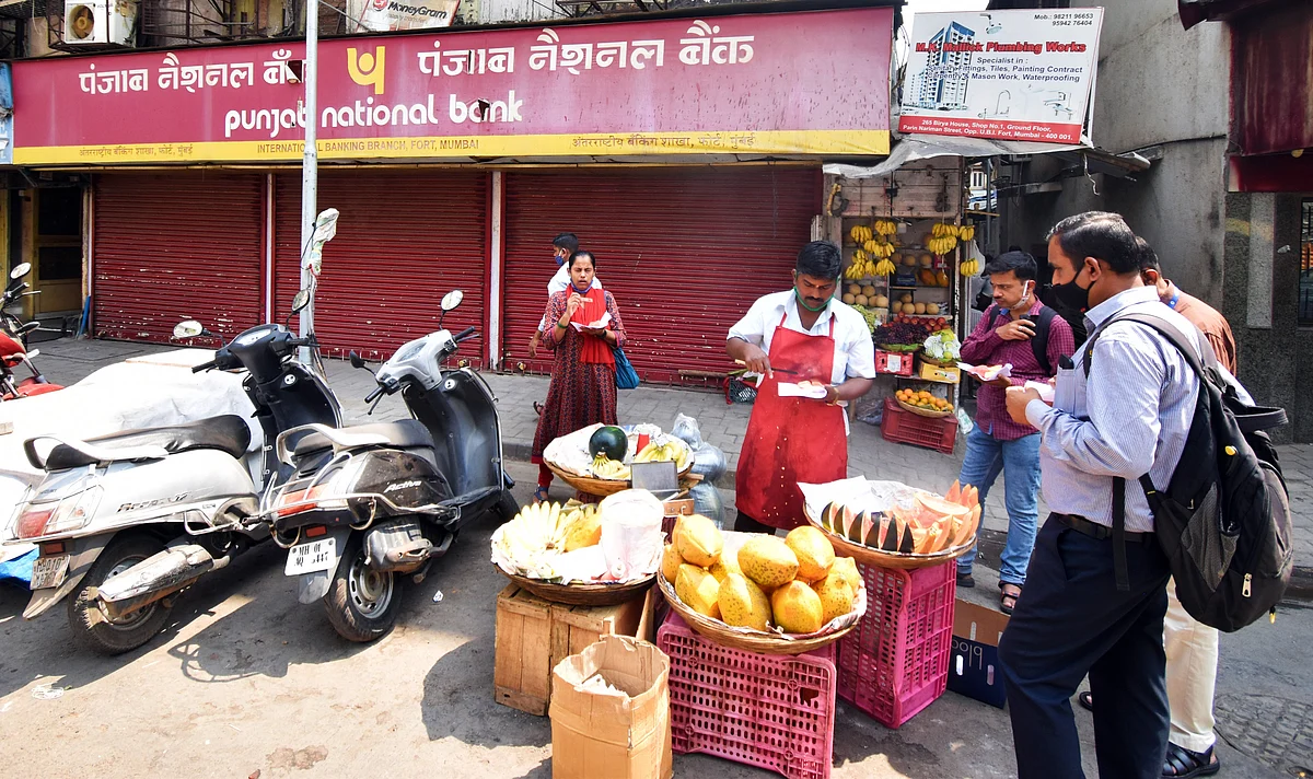 People eating fruit at a street side stall in Mumbai against the backdrop of a closed PNB Bank. Maharashtra has emerged with a positivity rate of 16%.