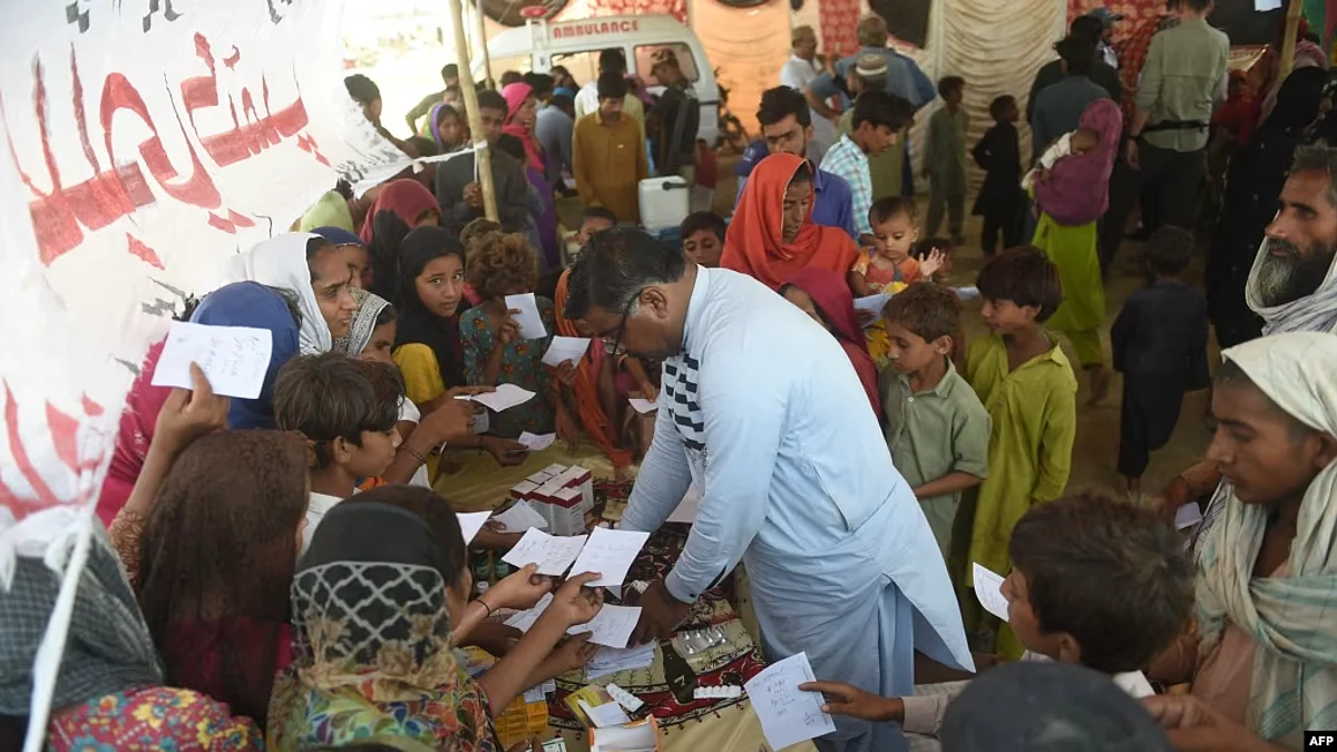 FILE - Families displaced by floods gather around a paramedic at a makeshift medical camp set in Dadu district, Sindh province in Pakistan on Sept. 27, 2022.