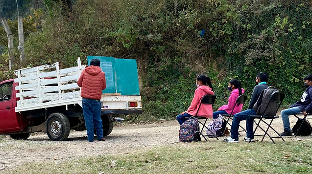 En las fotos se ve al maestro mientras da clases a sus alumnos al aire libre en una camioneta donde carga el pizarrón y las sillas (Foto Twitter: @vickolvera)