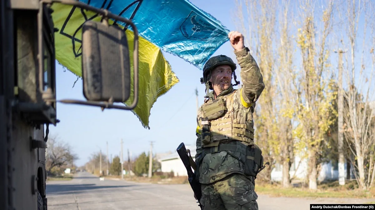 A soldier holds a weathered Ukrainian flag as the sun begins to set on the freshly recaptured town of Snihurivka, near Kherson.