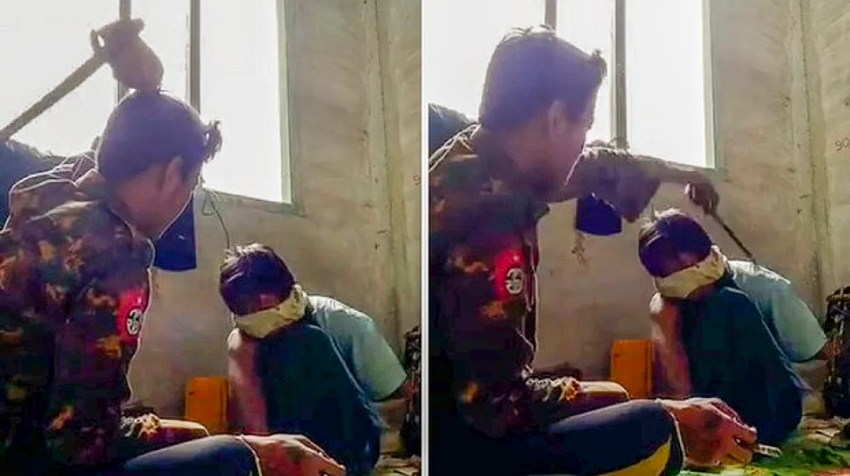 A man in a Myanmar military jacket strikes his captive with a rod as he asks the man if he is a member of the People’s Defense Force.