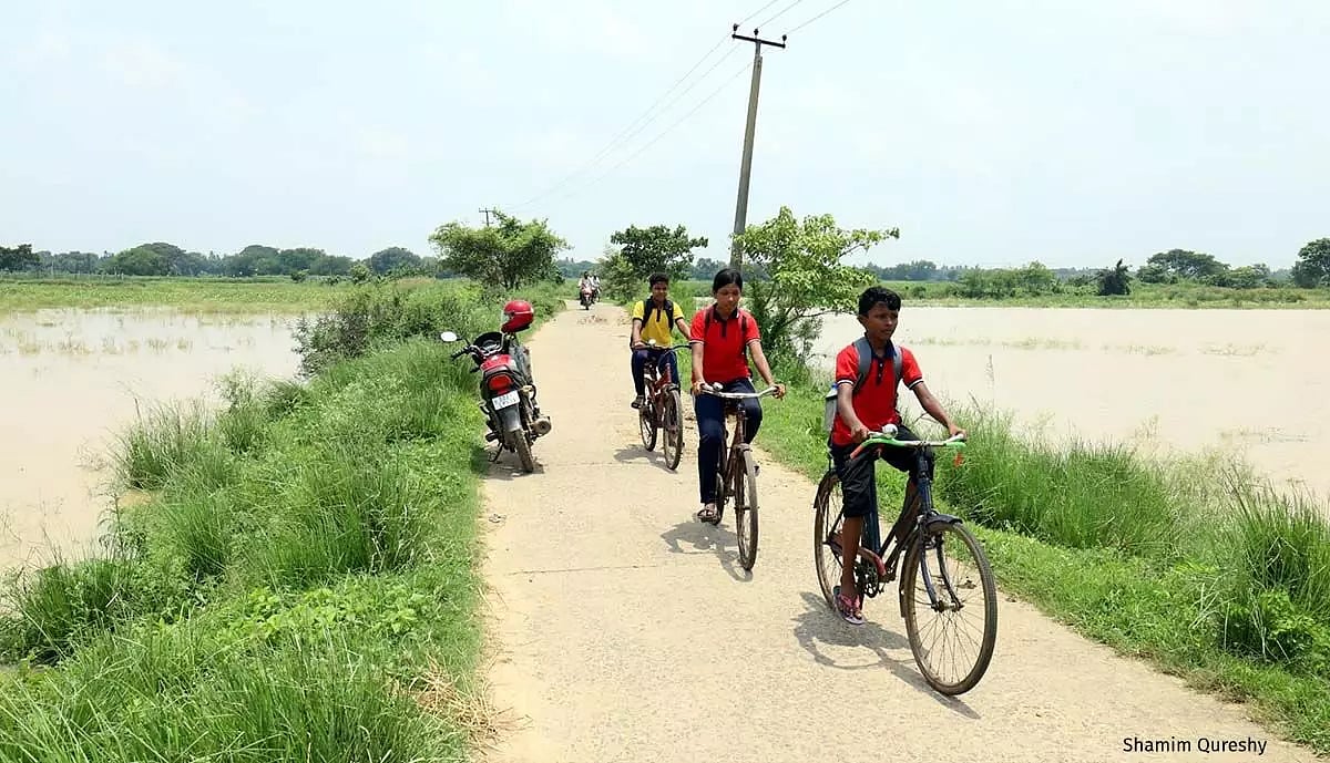 School children cycle down a road flanked by flood-submerged fields in Kujang block of Jagatsinghpur district in Odisha.