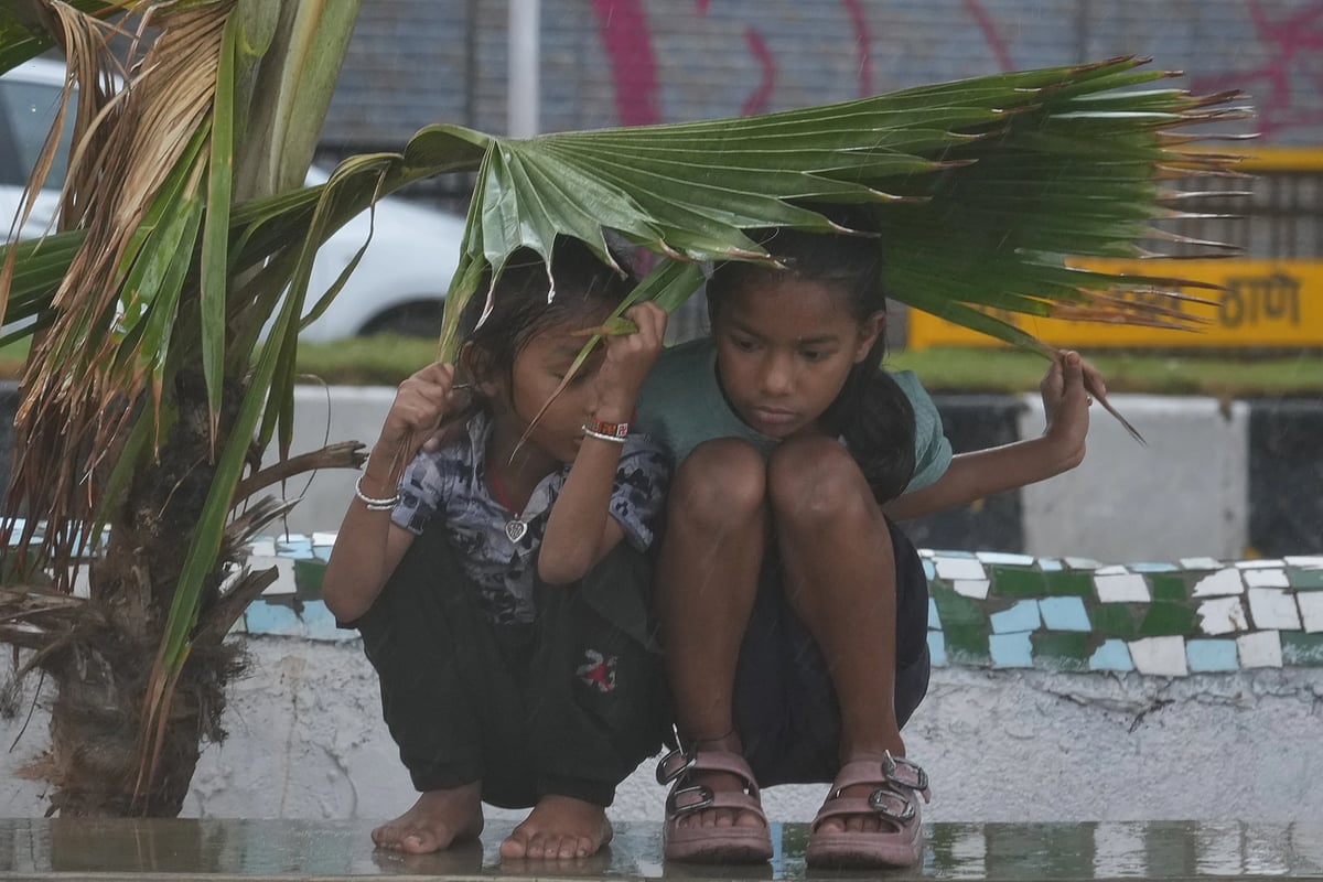 Girls take shelter under palm leaves during a monsoon shower in Mumbai. (AP Photo/Rafiq Maqbool)