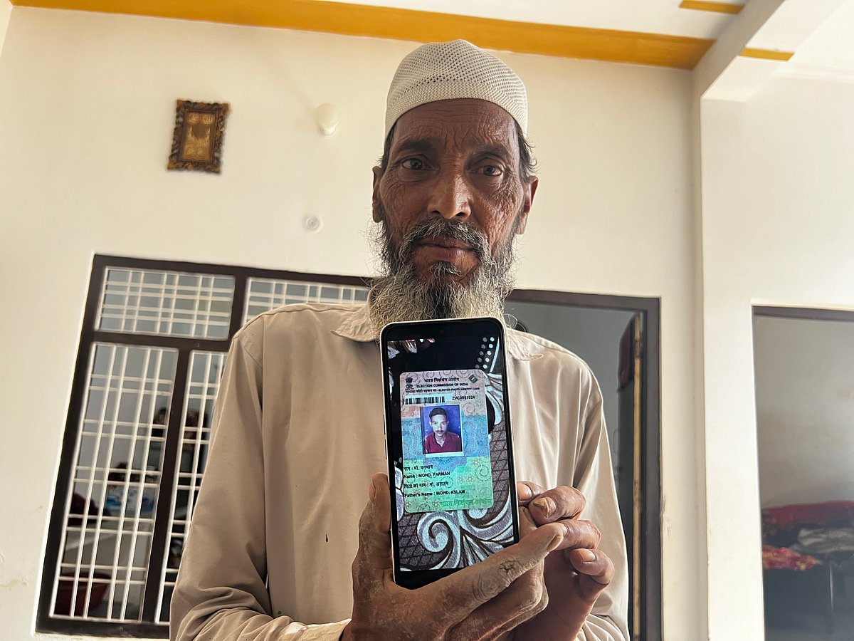 Farman's father holding up a photo of his son's voter ID card