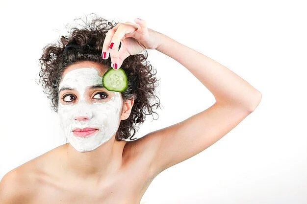 beautiful young woman with face mask holding cucumber slice against white background23 2147901182