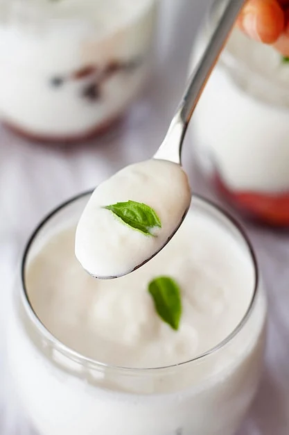 close up hand holding spoon with yogurt 23 2148660441