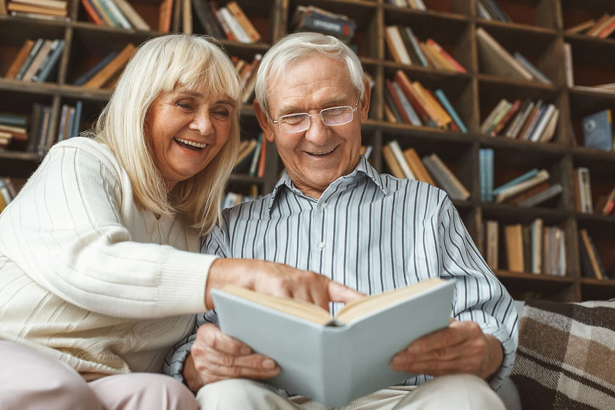 Senior couple smiling and reading a book by sitting on the couch
