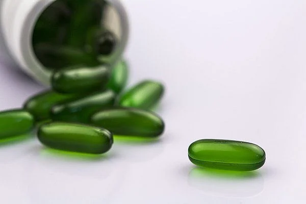 Green capsules in white bottle containing medicine aspirin and care