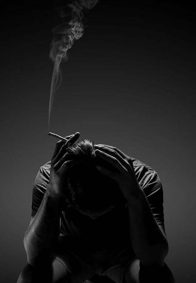 Cigarrillo que fuma del hombre deprimido que se sienta en silla en negro Foto Premium