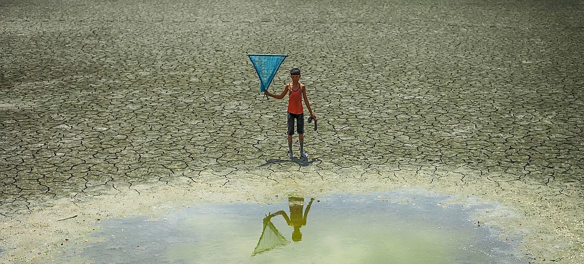 A young boy stands in front of a waterhole in a drought zone in Bangladesh