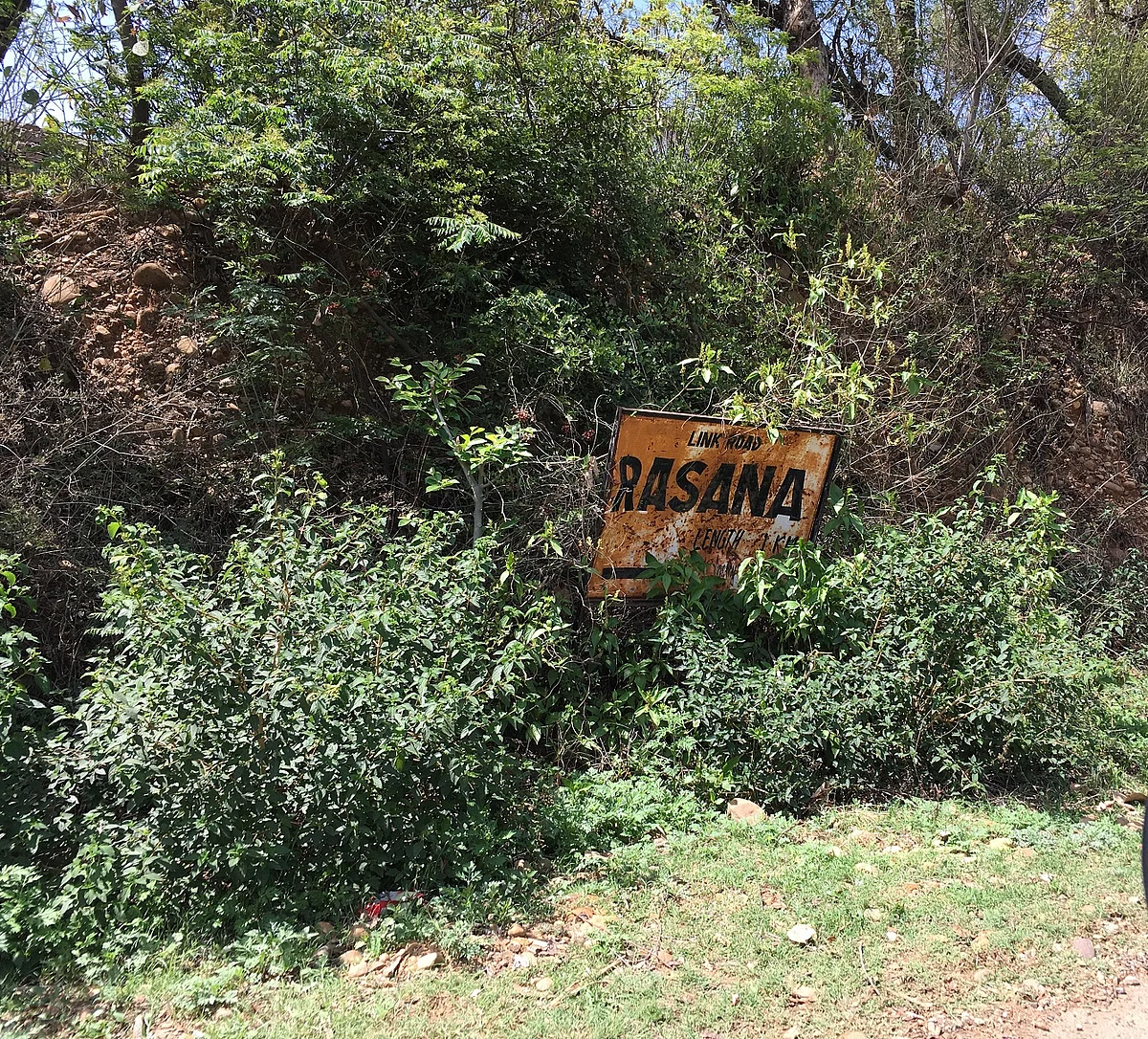 A battered iron board announces the entry to Patta Rasana village