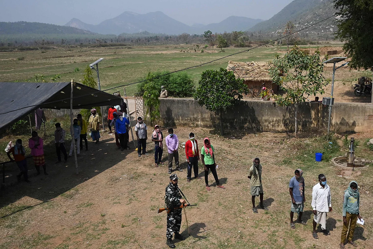 paramilitary personnel assists voters waiting to cast their vote outside a polling station during Phase 1 of West Bengal's legislative election in Purulia district on March 27, 2021.