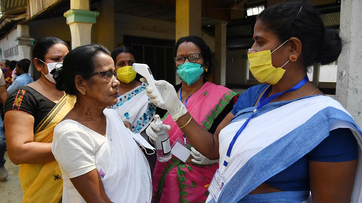 A health worker checks the body temperature of a voter, as a preventive measure against the COVID-19 coronavirus, before casting her ballot during Phase 1 of Assam's legislative election at a polling station in Koliabor, some 186 km from Guwahati on March 27, 2021.