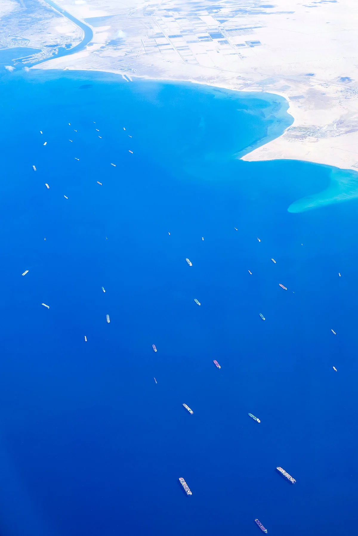 An aerial view taken from the porthole of a commercial plane shows ships stranded in the Red sea, as the Taiwan-owned MV 'Ever Given' (Evergreen) container ship, a 400-metre- (1,300-foot-)long and 59-metre wide vessel, remains lodged sideways on Egypt's Suez Canal ,impeding all traffic across the waterway, on March 27, 2021