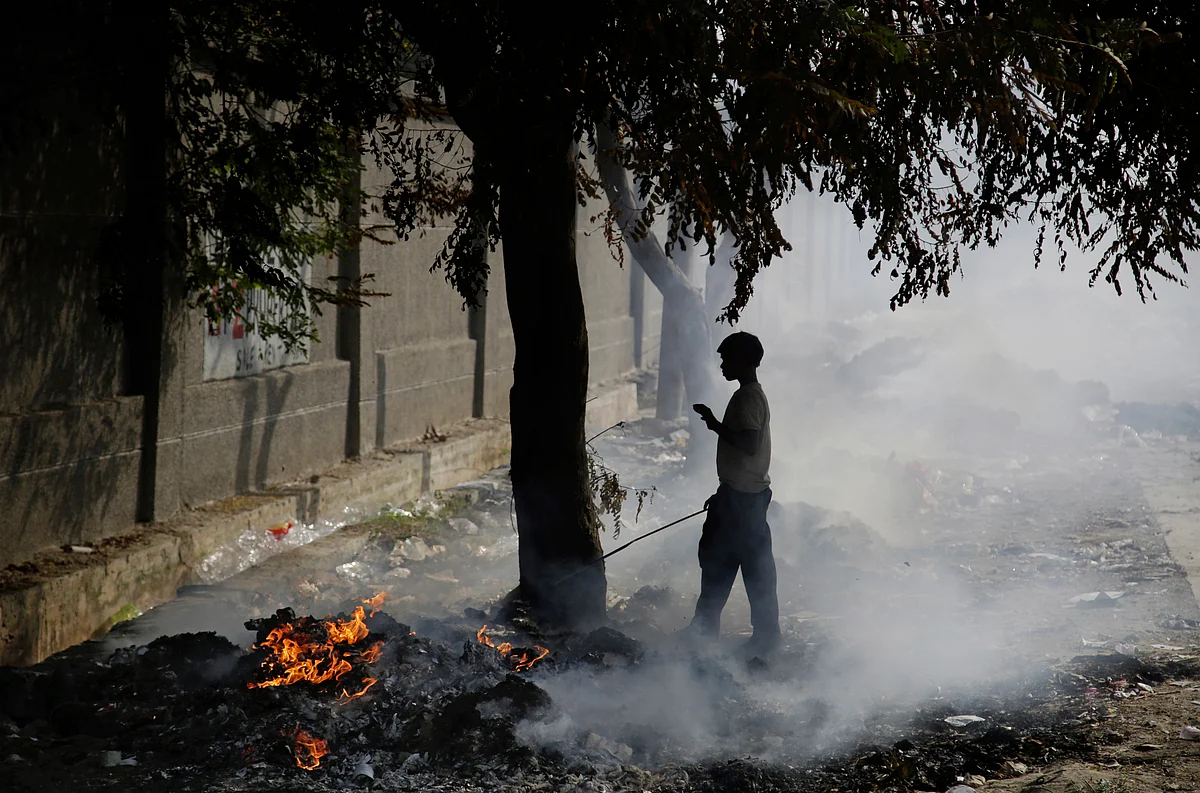 A ragpicker boy stand next to burning garbage on the outskirts of Delhi.