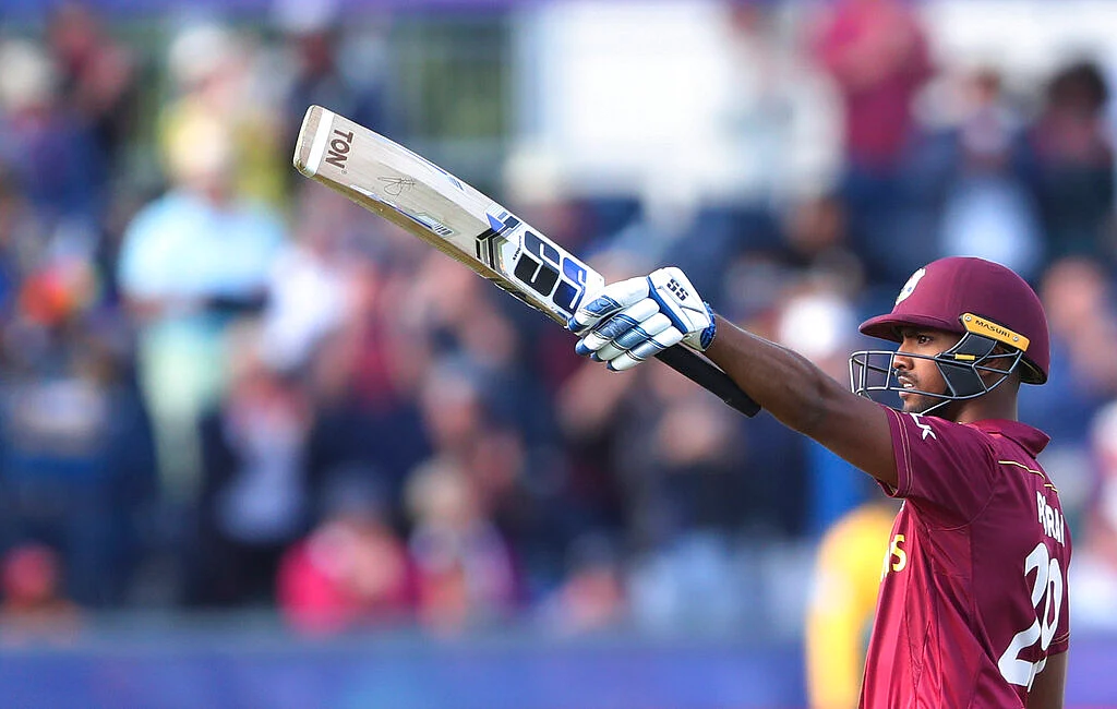 West Indies' batsman Nicholas Pooran raises his bat to celebrate scoring a century.