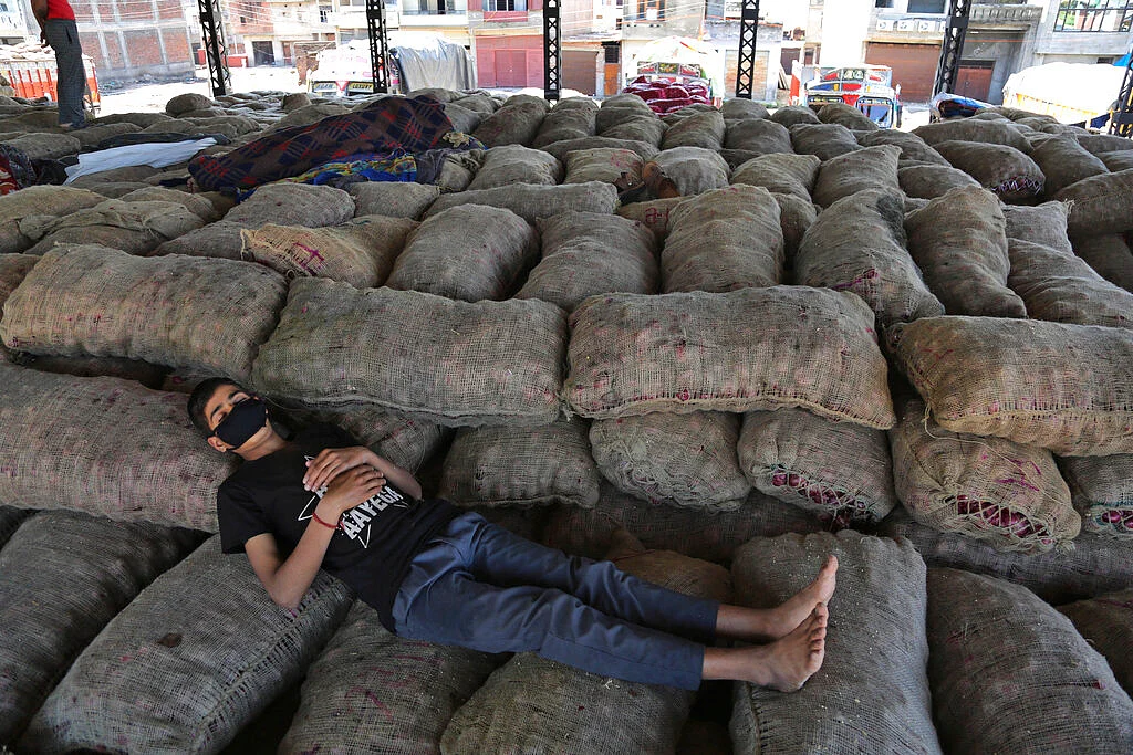 An Indian laborer sleeps on sacks of onions at a market during lockdown in Jammu, India.