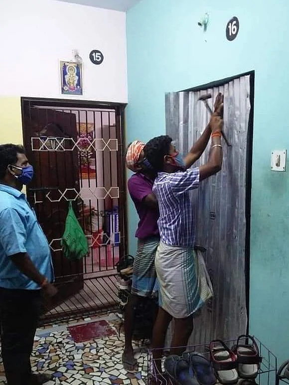 வீட்டின் கதவில் தகரமடிக்கும் நகராட்சி ஊழியர்கள்