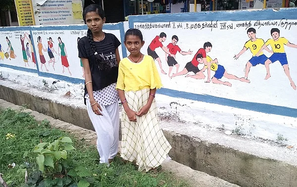 தாங்கள் வரைந்த ஓவியத்தை சுவரில் காணும் மாணவிகள்