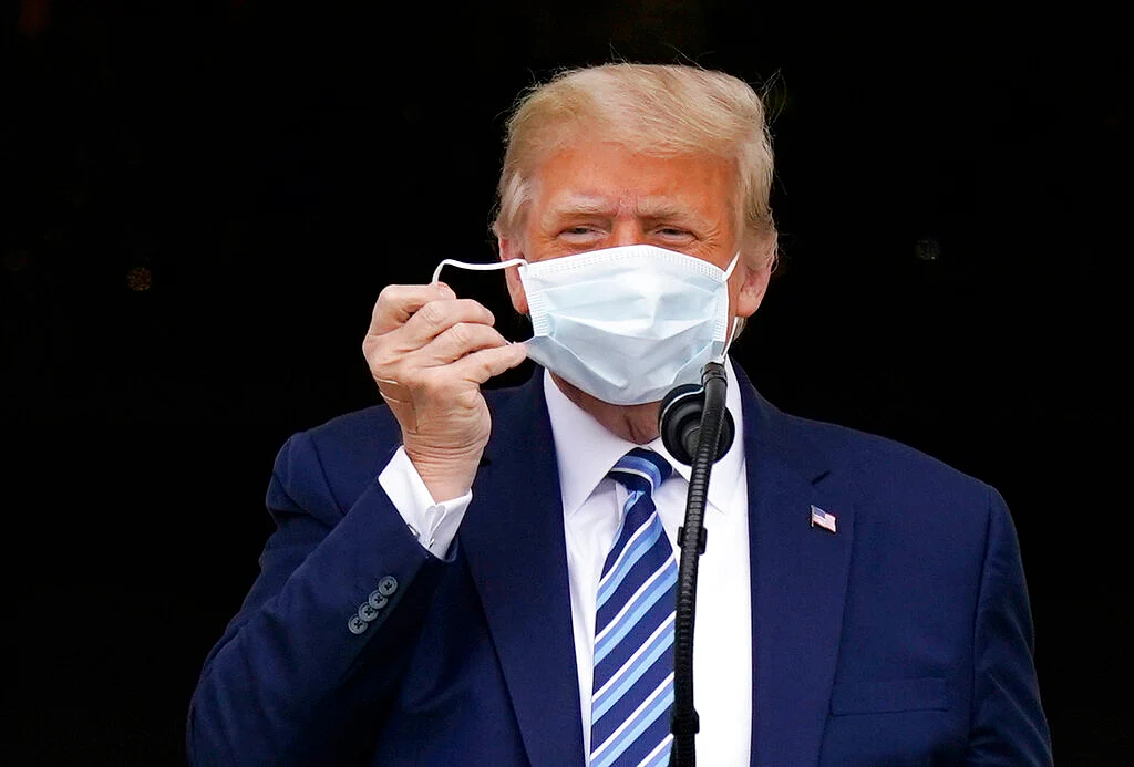 US President Donald Trump removes his face mask to speak from the Blue Room Balcony of the White House to a crowd of supporters