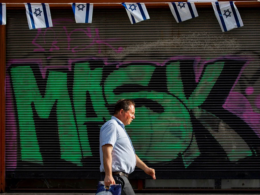 A man without a face mask walks by a "mask" graffiti
