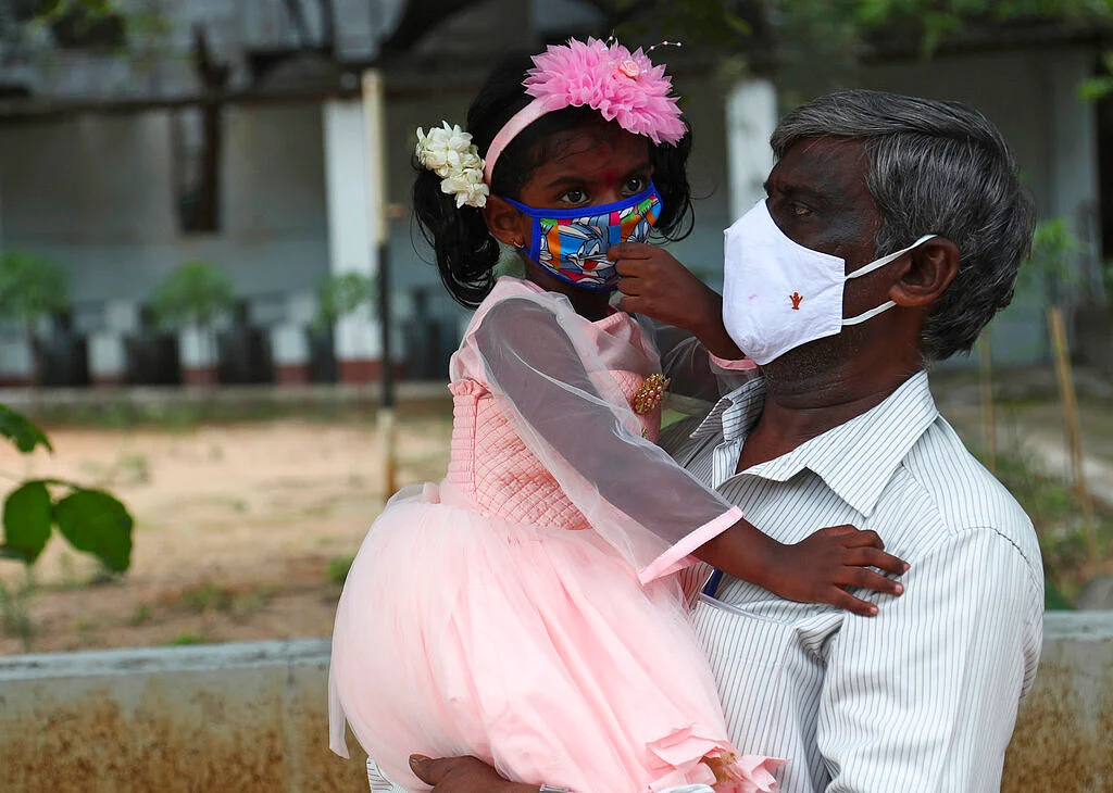 Rewind 2021: கோவிட் -19 டெல்டா, லாக்டௌன், ஒமிக்ரான்; முடியல தலைவரே! | rewind of covid 19 infection and vaccination in india during 2021 14 A man carries his granddaughter wearing face masks as a precaution against the coronavirus as he arrives to receive the Covaxin COVID-19 vaccine during a special vaccination drive in Hyderabad