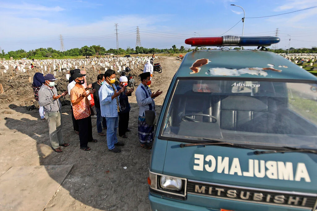 People pray outside an ambulance carrying the body of a relative who died from the coronavirus before the burial at a cemetery in Surabaya, East Java, Indonesia
